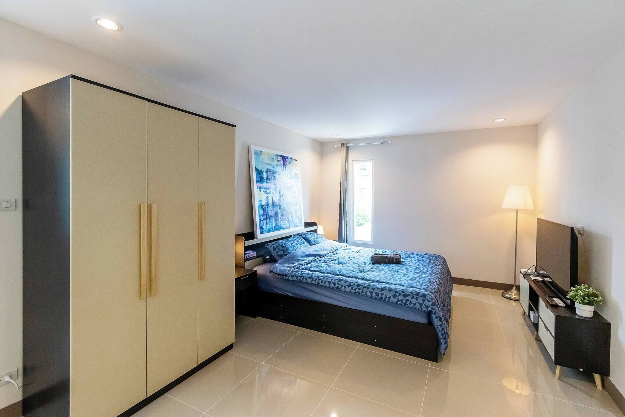 A bedroom with a bed, wardrobe, bedside table, lamp, and a painting on the wall.