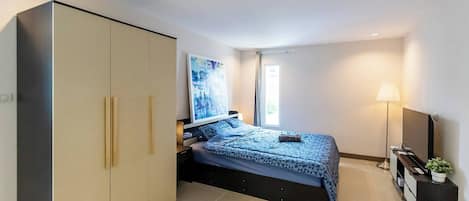A bedroom with a bed, wardrobe, bedside table, lamp, and a painting on the wall.