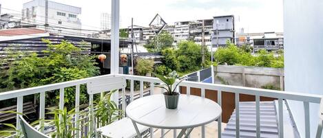 A balcony with a white table and chairs, surrounded by potted plants.
