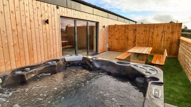 A hot tub area with a wooden deck and a patio table.