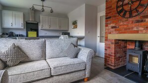 A living room with a grey sofa, a brick fireplace, and a kitchen in the background.