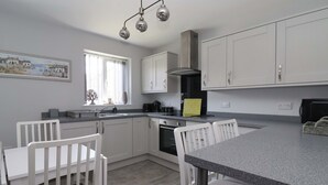 A modern kitchen with white cabinets, a granite countertop, and a dining area with white chairs.