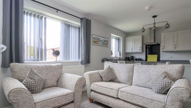A living room with two grey sofas, a coffee table, and a dining area with a kitchen in the background.
