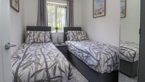A bedroom with two single beds, a window with curtains, a radiator, and a small potted plant.
