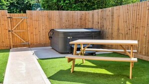 A backyard with a wooden picnic table, a hot tub, and a concrete pathway. - Wonderful  villa for 6 guests with hot tub, WIFI and pets allowed (Cirencester)