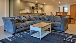 A modern living room with a sectional sofa, a wooden coffee table, and a kitchen in the background. - Wonderful  villa for 6 guests with hot tub, WIFI and pets allowed (Cirencester)