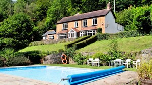 Una casa amb piscina, envoltada de vegetació exuberant i una paret de pedra.