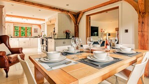 A dining area with a wooden table set for six, surrounded by white chairs.