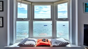 Une fenêtre en saillie donnant sur la mer, un lit avec des oreillers et un tableau encadré au mur.