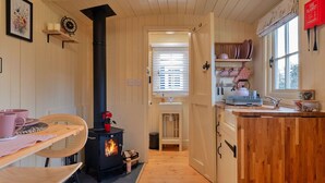A cozy kitchen with a wood-burning stove, wooden cabinets, and a window with blinds. - Beautiful  villa for 2 people with WIFI and pets allowed (Brackley)