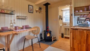 A cozy kitchen with wooden walls, a black stove, and a dining area with a chair and table. - Beautiful  villa for 2 people with WIFI and pets allowed (Brackley)