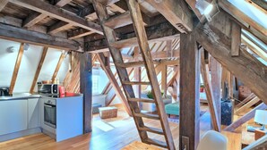 A loft-style room with exposed wooden beams, a kitchen area with modern appliances, and a cozy seating area with a ladder. - Lovely apartment for 3 guests with WIFI (Brackley)