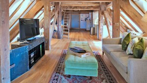 An attic room with a wooden ceiling, a television, a sofa, and a patterned rug. - Lovely apartment for 3 guests with WIFI (Brackley)