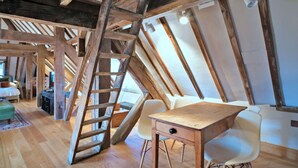 A loft bedroom with exposed wooden beams, a wooden ladder, a desk, and a chair. - Lovely apartment for 3 guests with WIFI (Brackley)