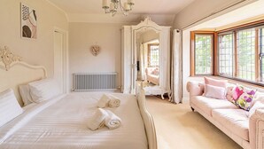 A bedroom with a large bed, a sitting area with a sofa, a mirror, and a chandelier. - Beautiful  villa for 16 guests with WIFI, hot tub and pets allowed (Aylesbury)