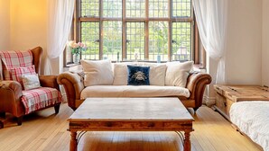 A cozy room with a wooden ceiling, a large window with a view of greenery, a brown leather sofa, a wooden table, and a plaid chair. - Beautiful  villa for 16 guests with WIFI, hot tub and pets allowed (Aylesbury)