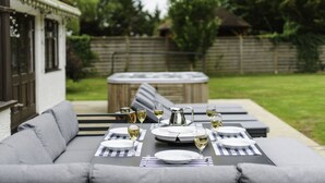 An outdoor dining area with a table set for four, a hot tub, and a sofa. - Beautiful  villa for 16 guests with WIFI, hot tub and pets allowed (Aylesbury)