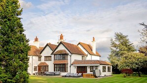 A large, white building with multiple chimneys, a well-maintained lawn, and outdoor seating. - Beautiful  villa for 16 guests with WIFI, hot tub and pets allowed (Aylesbury)