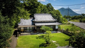 A traditional Japanese house with a tiled roof, surrounded by lush greenery and a clear view of a mountain in the background. - OMISHIMA SPACE HANARE (Imabari)