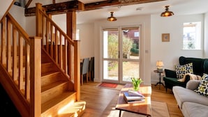 A wooden staircase leading to a room with a green sofa, a small table with books, and a door to a garden. - Wonderful  villa for 4 guests with WIFI, terrace and pets allowed (Chilton Foliat)