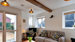 A cozy living room with a sofa, a coffee table, and a chair. There are windows with blinds, a lamp, and a ceiling fan. - Wonderful  villa for 4 guests with WIFI, terrace and pets allowed (Chilton Foliat)