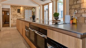 A modern kitchen with a stone wall, wooden cabinets, and a large island with a built-in oven. - Wonderful  villa for 19 people with WIFI, pool, TV and pets allowed (Stroud)