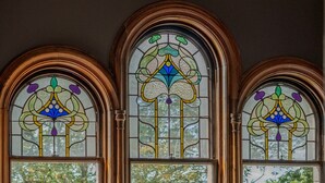 A room with three arched windows, a dining table with chairs, and a tufted sofa. - The Royal Tay Apartment - Stained Glass and River Views (Dundee)