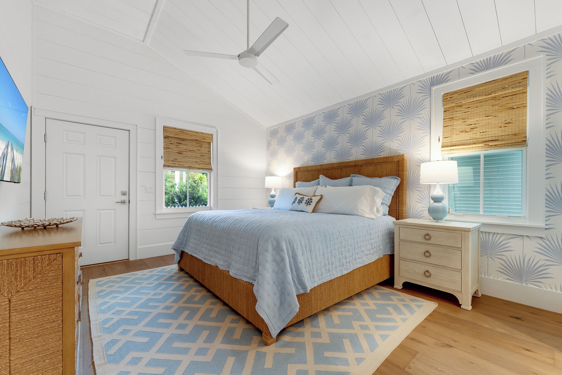 A bedroom with a bed, nightstands, a ceiling fan, and patterned wallpaper.