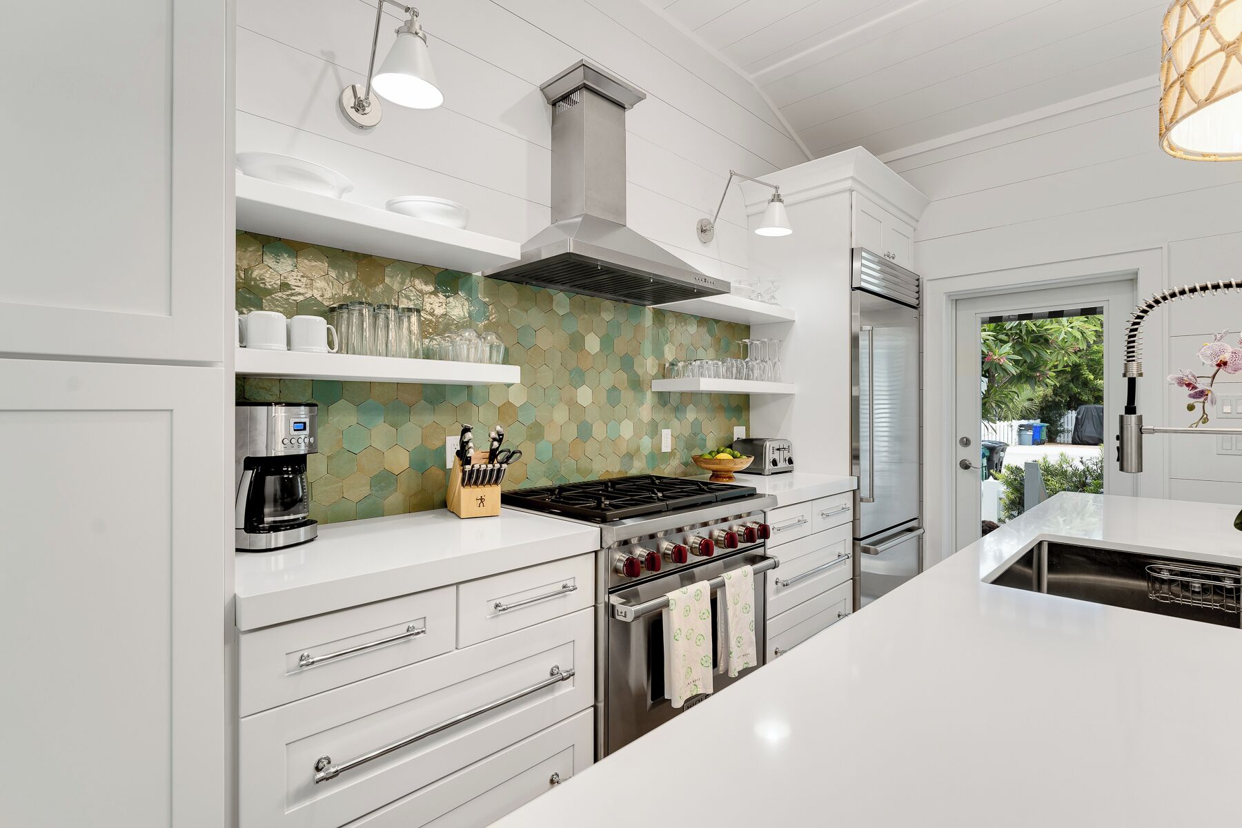 A modern kitchen with white cabinetry, a gas stove, an oven, a built-in coffee maker, and a backsplash with a geometric pattern.