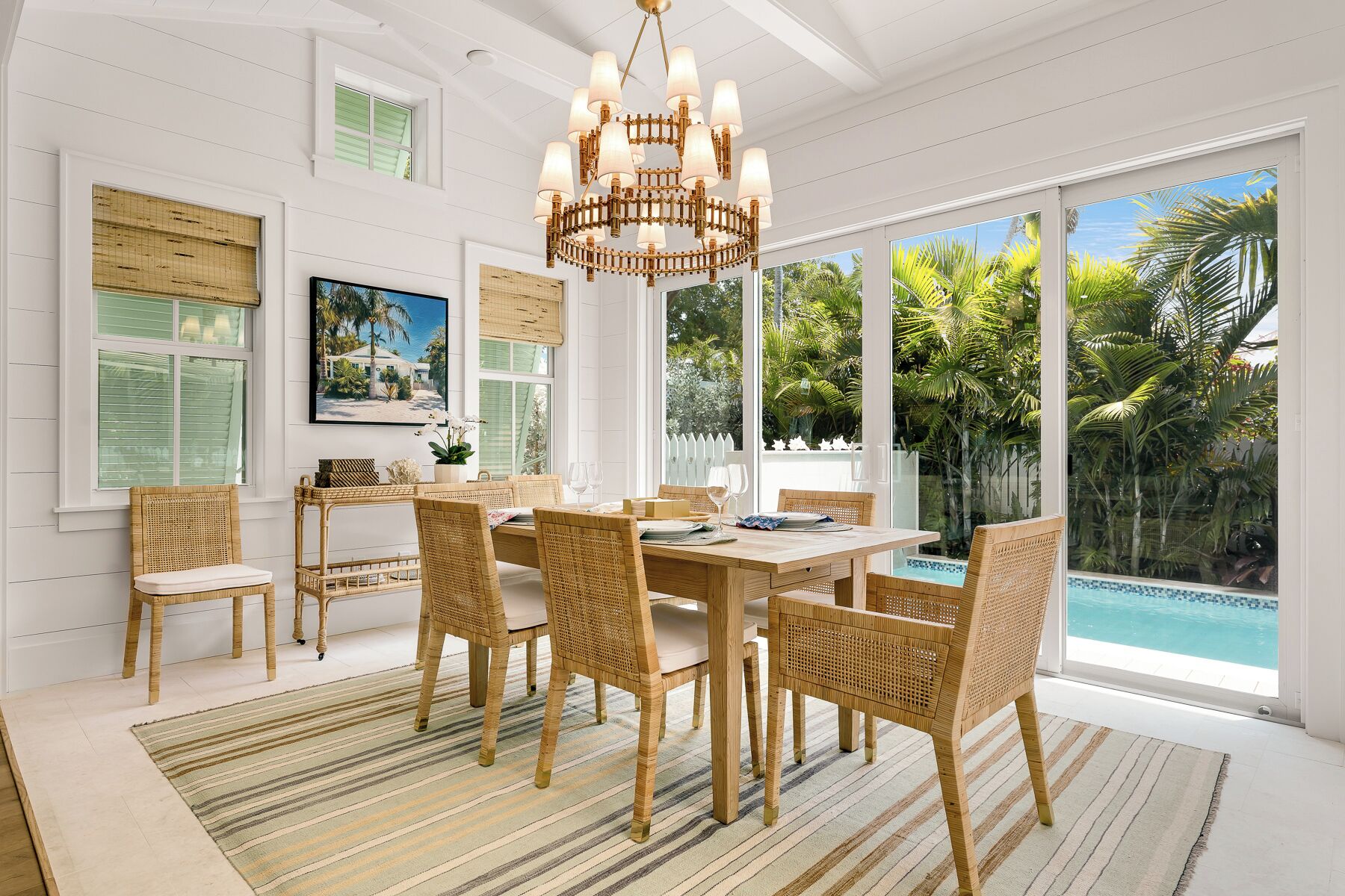 A spacious dining area with a large table and wicker chairs, overlooking a pool with tropical views.