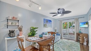 A modern living room with a dining area, a ceiling fan, a television, and a view of the outdoors. - A SEAGLASS PARADISE ~ Charming 2 BR/1 Ba 1st Floor Condo in Truman Annex! (Key West)