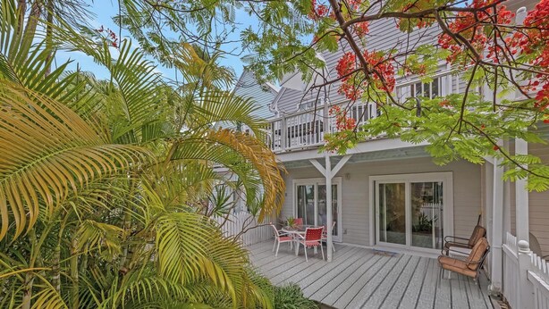 A two-story house with a wooden deck, a balcony, and a patio area with outdoor furniture. - A SEAGLASS PARADISE ~ Charming 2 BR/1 Ba 1st Floor Condo in Truman Annex! (Key West)