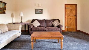 A living room with a brown leather sofa, a wooden coffee table, a beige sofa, a lamp, and a wooden door.