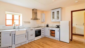 A modern kitchen with white cabinetry, a built-in oven, a stove, and a large window with blinds.