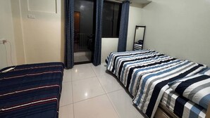A bedroom with two beds, a window with curtains, a mirror, and a door leading to another room. - Cozy Brenthill Condo in Baguio City - Entire House Rental (Baguio)