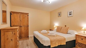 A bedroom with a bed, wooden wardrobe, bedside tables, and a ceiling light fixture.