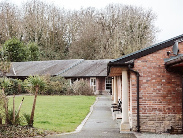 A building with a brick exterior, a covered porch with chairs, and a grassy area in front.