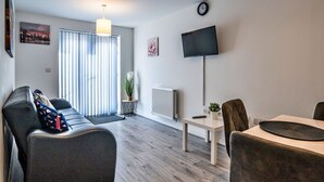 A modern living room with a sofa, a dining table, and a TV mounted on the wall. - Cosy apartment for 3 guests with WIFI (Birmingham)
