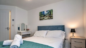 A neatly made bed with a teal blanket, a bedside lamp, and a painting of a forest scene on the wall. - Cosy apartment for 3 guests with WIFI (Birmingham)