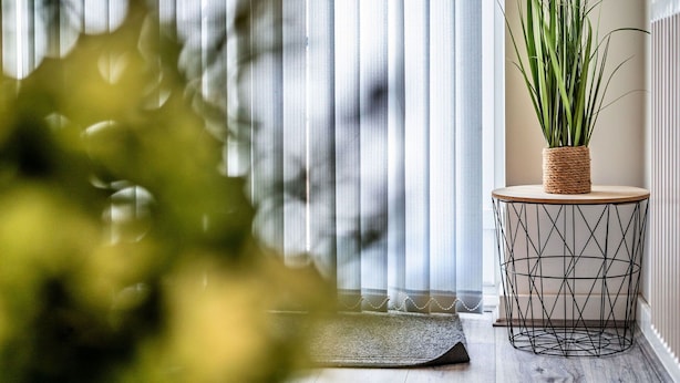 A room with a large window covered by sheer curtains, a round side table with a woven basket holding green plants, and a geometric wire floor lamp. - Cosy apartment for 3 guests with WIFI (Birmingham)