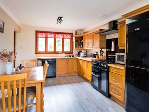A kitchen with wooden cabinets, a stove, a refrigerator, and a dining area with a table and chairs.