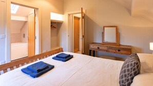 A bedroom with a bed, a wooden dresser, a mirror, and a bathroom visible through an open door.
