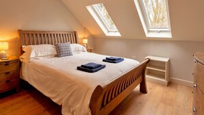 A bedroom with a sloped ceiling, two skylights, a wooden bed, bedside lamps, and a small bedside table. - Beautiful  villa for 8 people with WIFI, TV and pets allowed (Alcester)