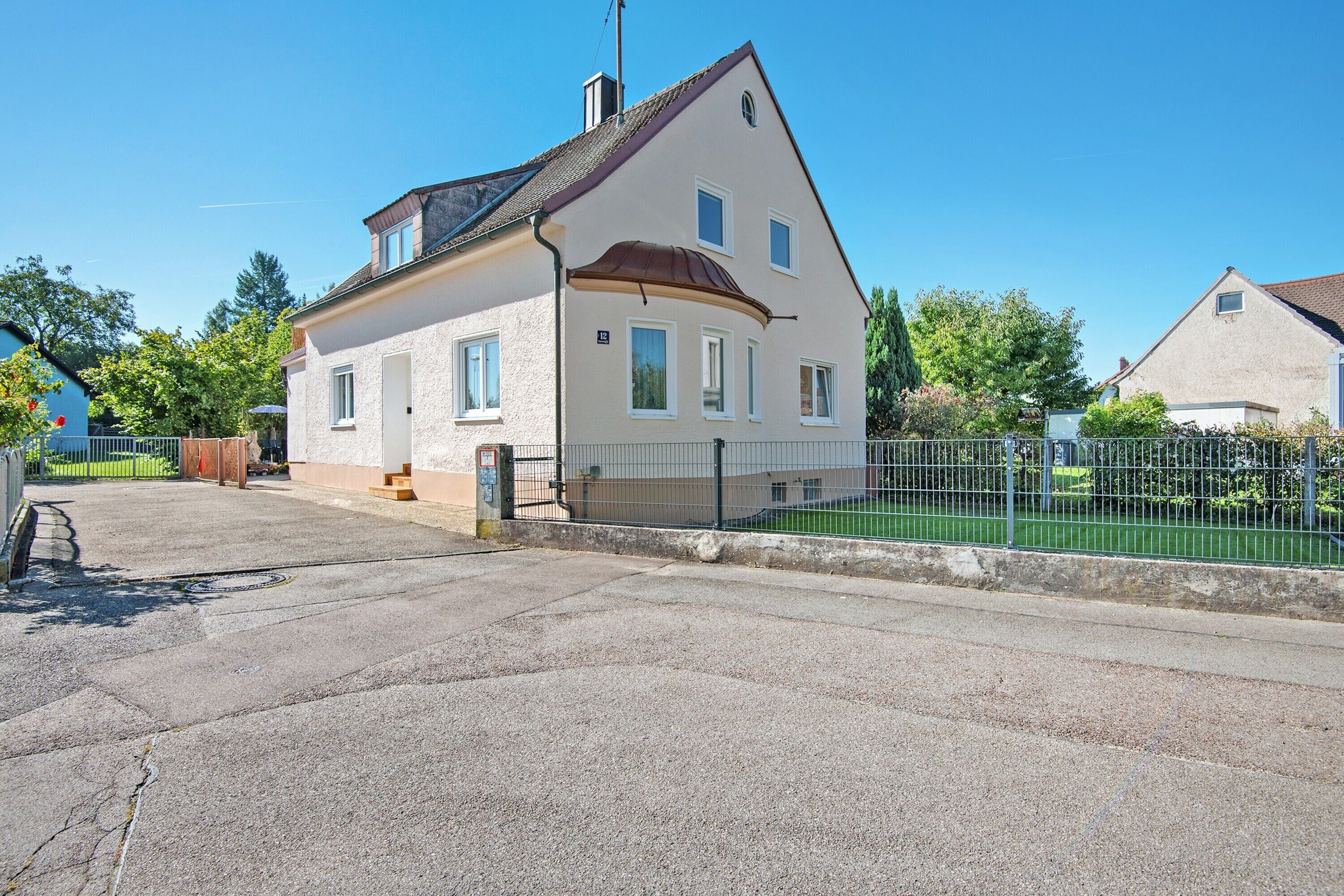 Ein zweistöckiges Haus mit geneigtem Dach, einem eingezäunten Garten und einem gepflasterten Einfahrt.