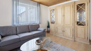 Una sala de estar con un sofá, una mesa de centro de vidrio, armarios de madera y un ventanal con cortinas translúcidas.