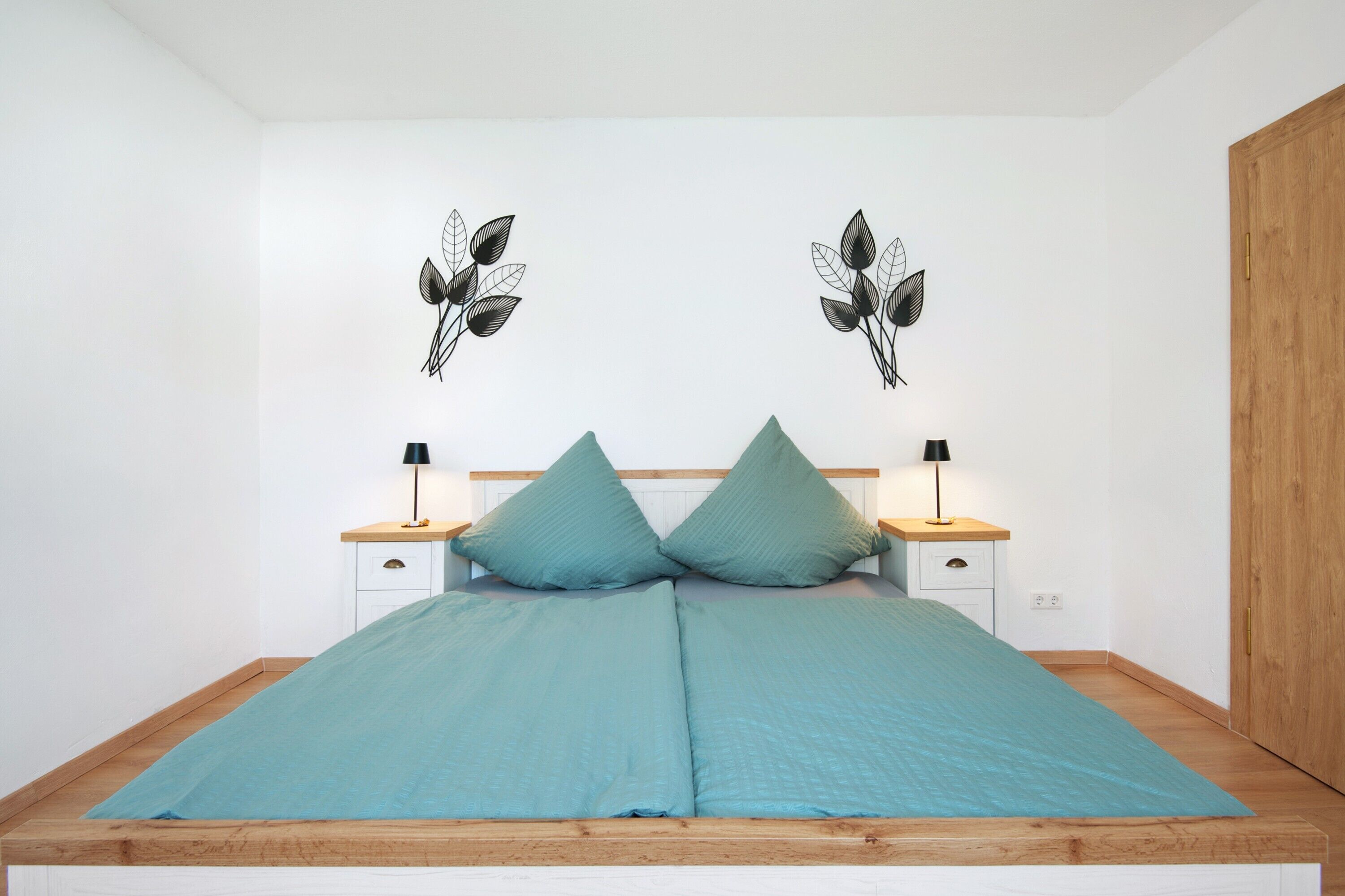 Una cama con dos almohadas, una mesita de noche con una lámpara y un adorno en la pared.