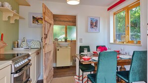 A compact kitchen with a wooden door, a sink, and a dining area with teal chairs and a wooden table. - Beautiful  villa for 4 people with terrace (Shrawardine)