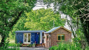 A small, rustic cabin with a blue exterior and a brick extension, surrounded by lush greenery. - Beautiful  villa for 4 people with terrace (Shrawardine)