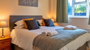 A neatly made bed with white linens and a patterned throw, a bedside lamp, and a wall-mounted artwork. - Wonderful  villa for 5 people with WIFI, TV and pets allowed (Burnham-on-sea)