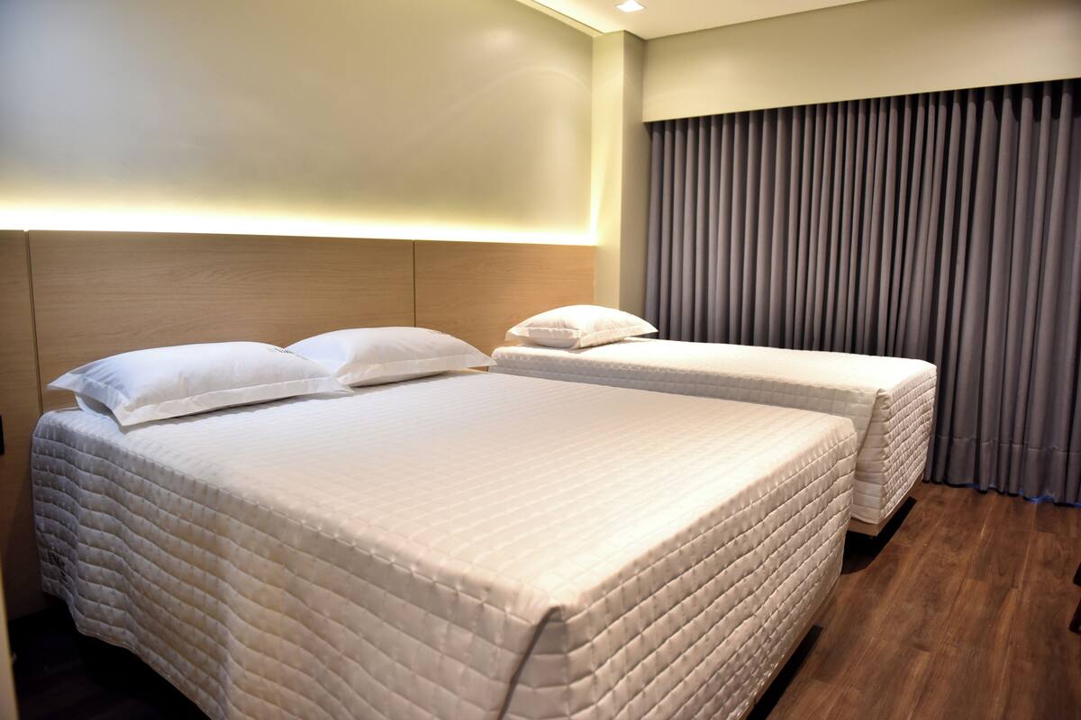 Une chambre d’hôtel avec deux lits, une tête de lit en bois et une grande fenêtre avec des rideaux.